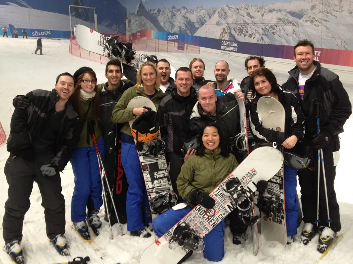 About a dozen of the team in ski gear with snowboards on an indoor slope