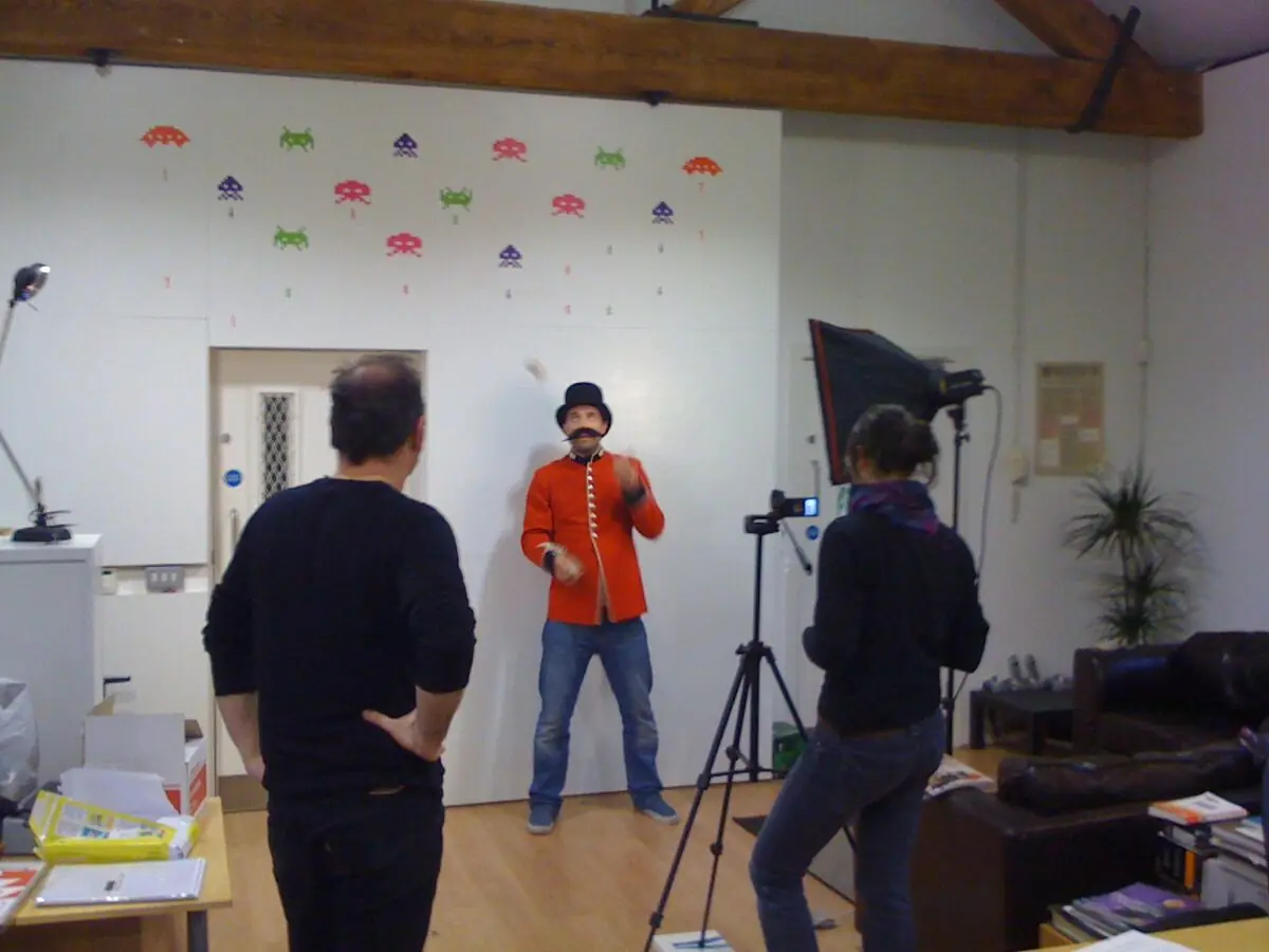 A video shoot in the Clapham studio: one of the team in a red guardsman’s jacket and top hat under the lights, Space Invader decals on the wall