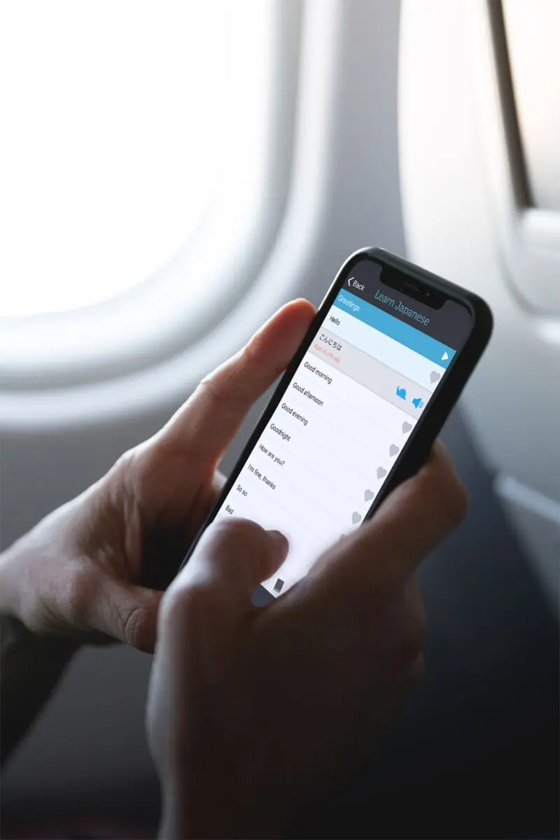 Hands holding an iPhone running a Learn phrasebook app, by an aircraft window
