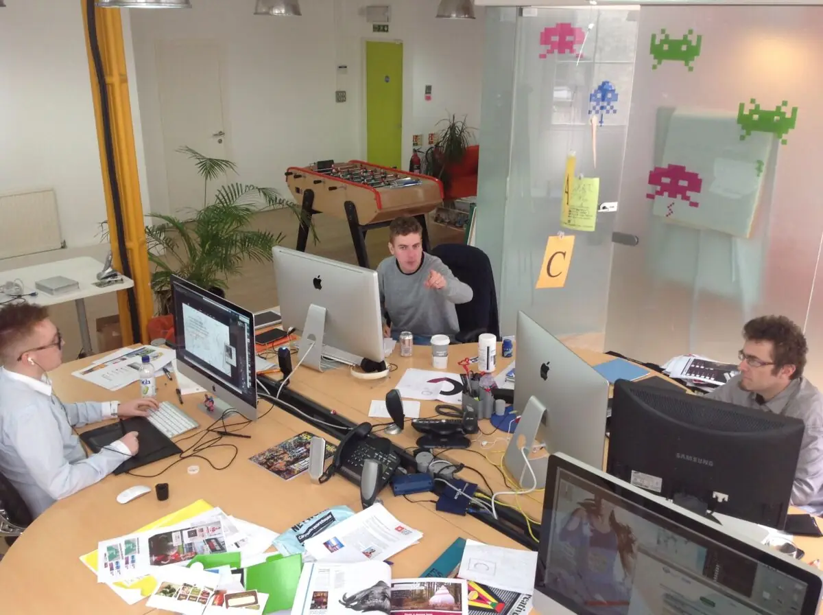 The team at the round desk with iMacs, Space Invader decals and C-O-D-E letter cards on the glass