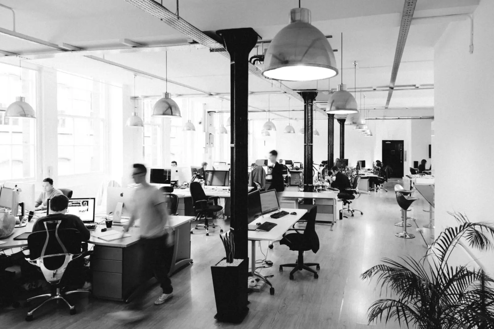 The open-plan studio floor in black and white: iron columns, pendant lamps and people at their desks