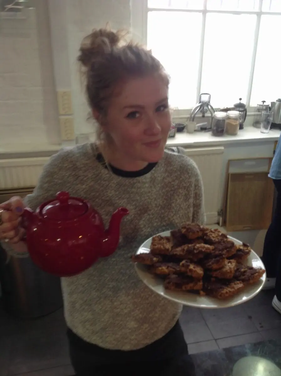 A member of the team holding a red teapot and a plate of homemade cakes