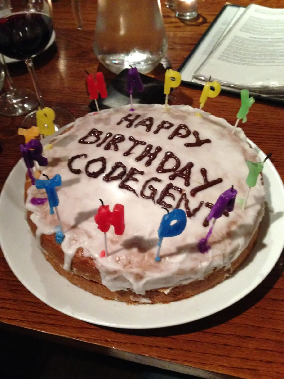 A homemade iced cake reading Happy Birthday Codegent, with letter candles