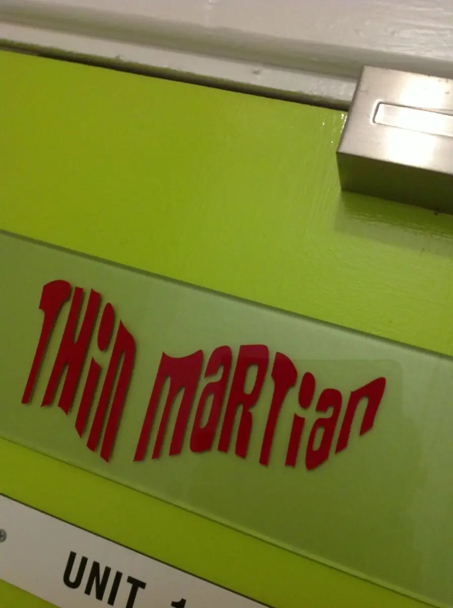 The red Thin Martian logo on the green unit sign at the entrance