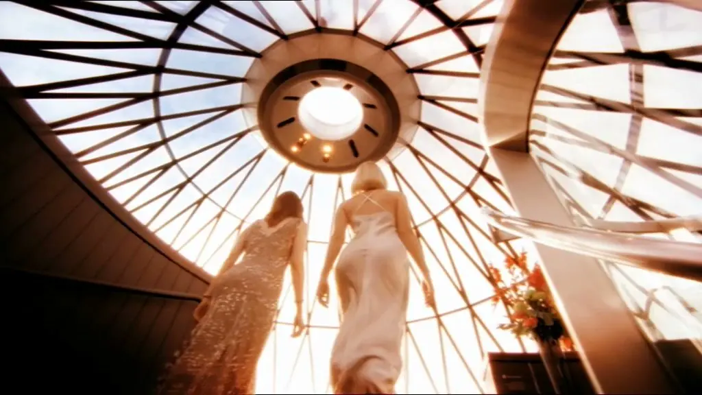 Two women in evening dresses climbing the spiral stair into the sunlit dome